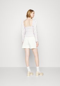 Calções brancos, blusa lilás e branca com mangas bufantes e corpete franzido, saia em camadas e sapatos de salto plataforma bege combinados com meias brancas.