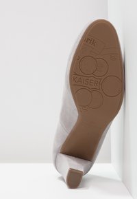Chaussure à talon haut en daim gris avec un bout effilé et un talon fin. La semelle présente un marquage en relief et des détails texturés.
