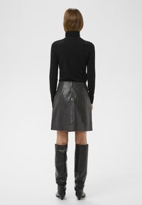 Top negro de cuello alto combinado con una falda corta de cuero negra. Botas negras hasta la rodilla. Textura suave y detalles de diseño minimalista.