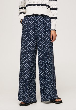 Pantalons larges bleu marine avec un motif géométrique blanc, présentant une coupe ample et des poches latérales. Portés avec un pull texturé crème.