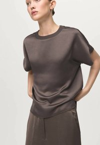 Brown short-sleeve top with a smooth texture, round neckline, and relaxed fit, paired with matching high-waisted trousers.
