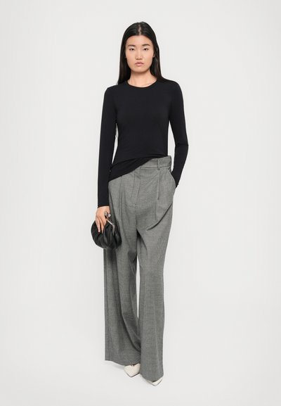 Black long-sleeve top paired with high-waisted, wide-legged grey check-pattern trousers and a black clutch bag. White pointed-toe shoes.