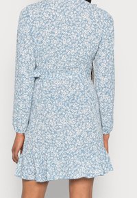 Modré květinové šaty s dlouhými rukávy a přiléhavým vrškem. Rozšířený volánový spodní lem, se vzorem bílých květin na světle modrém pozadí.