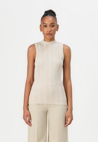 Hihaton beige ribbed neulepaita, jossa on korkea kaula-aukko ja tekstuuri, yhdistettynä löysästi istuviin kermanvärisiin housuihin.