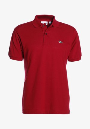 Sarkans polo krekls, izgatavots no kokvilnas, ar klasisku apkakli, īsām piedurknēm, divu pogu auklu un nelielu zaļu izšūtu logo uz krūtīm.