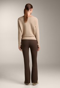 Beige bordás pulóver széles nyakkivágással, amihez testhezálló barna, bő szabású nadrág tartozik. Puha textúra látható; minimalista design díszítések nélkül.