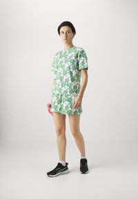 Zaļā lapu raksta īsām piedurknēm pierežģīta blūze un saskaņoti šorti; izgatavoti no viegla auduma. Iespējama apaļa kakla izgriezuma un smalki akcenti.