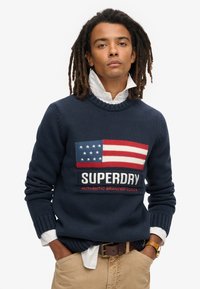 Maglione a maglia blu navy con design della bandiera americana nei colori rosso, bianco e blu, brandizzato "SUPERDRY" e con polsini e bordo a costine.
