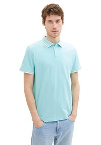 Polo bleu clair en tissu respirant, avec une patte de boutonnage à trois boutons, un logo brodé et des bordures blanches contrastées sur le col et les manches.