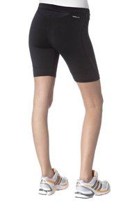 Bakifrån av en person som bär svarta ClimaCool träningsshorts och vita löparskor med orange och svarta detaljer.