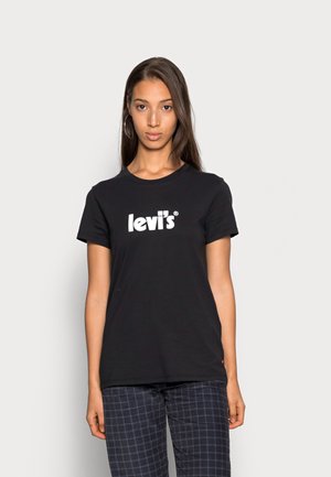 T-shirt en coton noir avec un logo Levi's blanc sur le devant, col rond, manches courtes et coupe décontractée. Modèle présenté avec un pantalon à carreaux.