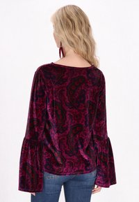 Top in velluto viola scuro con motivo paisley. Presenta maniche a campana e un ampio scollo, realizzato in un tessuto liscio e strutturato.