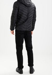 Svart pufferjacka med huva, med chevron-sömnad, tillsammans med svarta rakbenbyxor och svarta ankelstövlar.