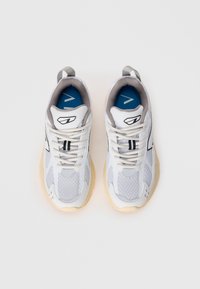 White and grey athletic shoes with mesh upper, round toe, lace closure, and beige sole. Features a blue insole and black logo detail.
