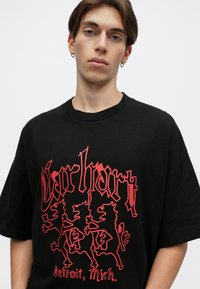 Czarna bawełniana koszulka z krótkim rękawem, z dużym czerwonym napisem graficznym i trzema figurami lwów, z okrągłym dekoltem.