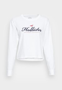 Vit långärmad kort sweatshirt med "Hollister" och "Southern California" tryckt i marinblått och rött. I bomullsmaterial med rund halsringning.