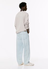 Lichtgrijze oversized sweatshirt met opgerolde mouwen, gecombineerd met lichtblauwe baggy jeans en crèmekleurige sneakers, gezien vanuit de achterkant.