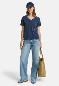 Marine v-hals t-shirt, lyseblå brede bukser, blå og hvide sneakers og en blød brun tote bag. Afslappet og behageligt outfit.