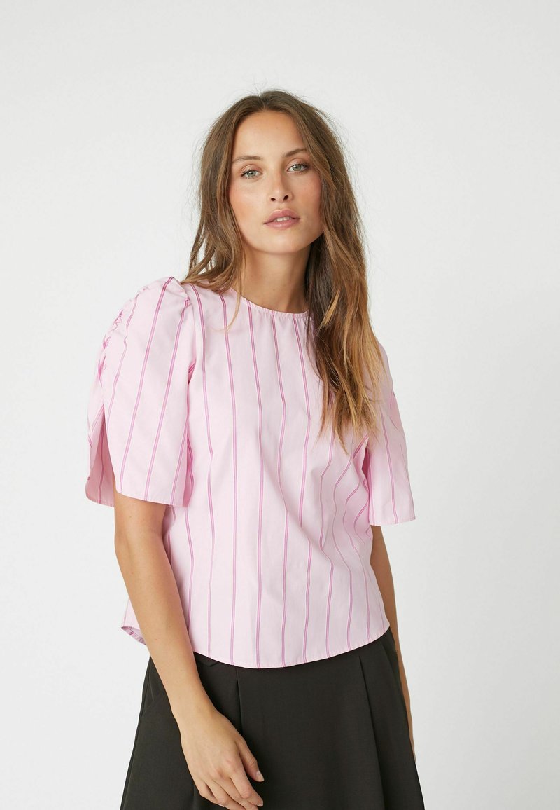 Blusa rosa chiaro a maniche corte con strisce verticali rosa. Tessuto morbido, scollatura rotonda e vestibilità leggermente ampia. Dettaglio delle maniche drappeggiate.