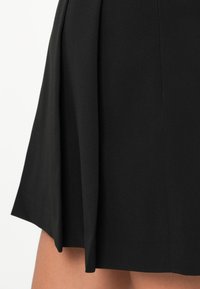 Fekete pliszé szoknya könnyű szövetből, sima textúrával, tiszta, szabott kinézettel, és diszkrét részletezéssel az alján.