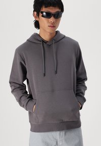 Grijze katoenen hoodie met verstelbare trekkoorden, voorzak en geribde manchetten, gecombineerd met zwarte zonnebril en lichtgekleurde shorts.