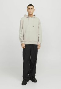 Light beige hoodie with a front pocket and drawstring, paired with loose black cargo pants featuring side pockets. Footwear is black, chunky.