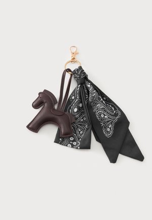 Guld nøglering med en brun læder hestevedhæng og et knyttet sort stofbandana med hvide paisley-mønstre.