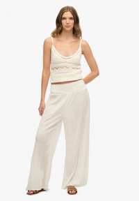 Top cortito de ganchillo blanco con escote en V y tirantes delgados, combinado con pantalones blancos sueltos y fluidos que cuentan con una cinturilla texturizada y detalles laterales.