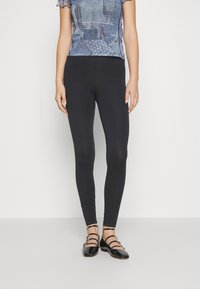 Leggings negros hechos de material elástico, diseño ajustado, con una textura suave. Combinados con una blusa de patrón de denim y zapatos de tiras negros.