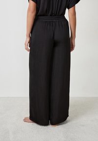 Zwarte wijde broek gemaakt van lichtgewicht stof. Heeft een elastische tailleband en een zachte textuur, valt losjes tot op de grond.