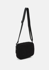 Black corduroy crossbody bag with rectangular shape, adjustable strap, and a zippered closure. Textured surface with ribbed pattern.