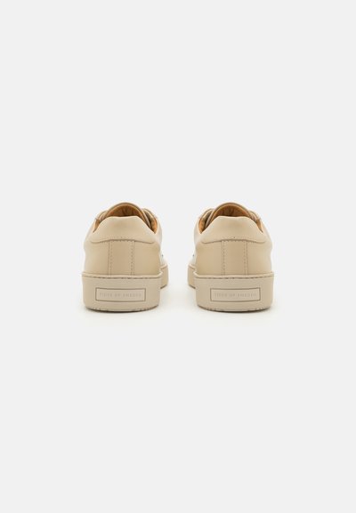 Beige leather sneakers with a smooth texture, featuring a low profile and a textured rubber sole. Branding is visible on the heel.
