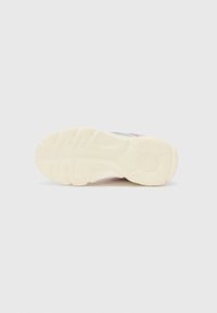 Suela de zapato de goma blanca texturizada, con patrones de banda de rodadura para agarre. El diseño incluye un logo circular y un acento de color a lo largo del lado.