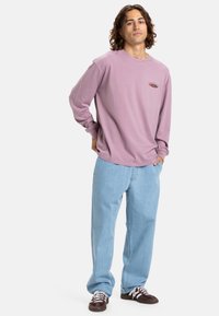 Langermet lavendel skjorte med liten grafikk, sammen med lyseblå posete jeans og brune joggesko med hvite lisser.