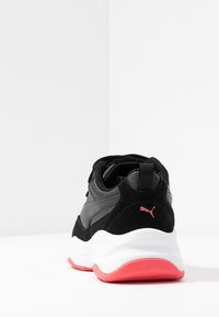 Černé a šedé tenisky s robustní bílou podrážkou a červenou vnější podrážkou, z pohledu zezadu, s červeným logem Puma na patě.