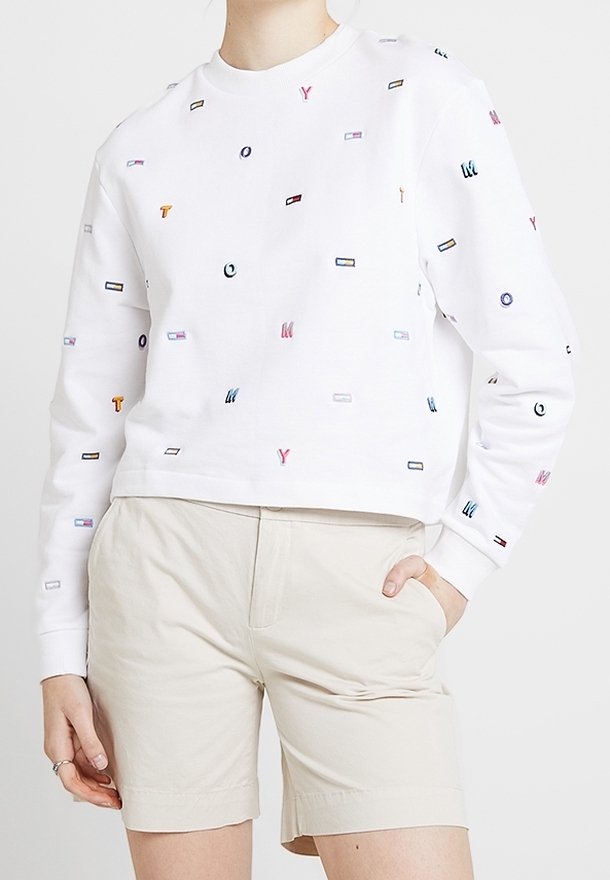Vit kortärmad sweatshirt med färgglada broderade bokstäver och former. Bärs med ljusbeiga shorts, vilket ger en avslappnad passform.