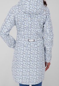 Lekka, wzorzysta kurtka z niebieskim kropeczkowym wzorem na białym tle, z zdobioną talią i kapturem. Gładka faktura.