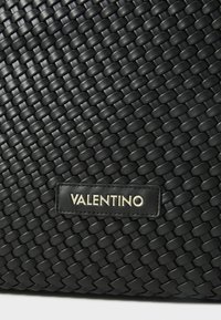 Borsa a tracolla in pelle intrecciata nera con una finitura testurizzata e una toppa rettangolare con il nome "Valentino" in lettere dorate.