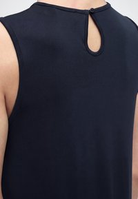 Πίσω όψη ενός ατόμου που φοράει μαύρο τοπ χωρίς μανίκια με μικρή τρύπα κλειδιού και κουμπί στο πάνω μέρος της πλάτης.