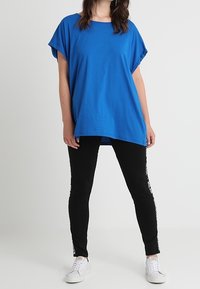 Modré oversized tričko z měkké látky s kulatým výstřihem, doplněné černými legínami s bílými potisky podél stran.