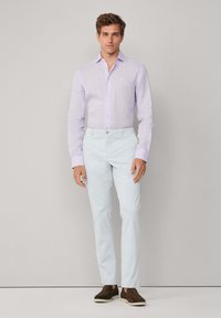 Helllila Leinenhemd mit Button-Down-Kragen, kombiniert mit blassen blauen Slim-Fit-Hosen und braunen Slippern. Schlichtes Design, strukturierter Stoff.