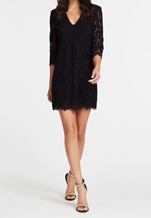 Robe en dentelle noire avec un col en V, des manches trois-quarts et un ourlet festonné. Associée à des sandales noires ornées de chaînes dorées.