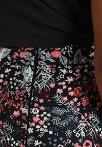 Falda con estampado floral sobre un fondo negro, que presenta rosas y hojas bordadas en rojo, rosa y azul. Detalle de cremallera en la parte de atrás.