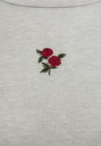 Grå ribbat tyg med rund halsringning har broderade röda rosor och gröna blad i bröstområdet.