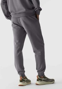 Graue Jogginghosen aus weichem Material, mit lockerer Passform, gerippten Bündchen und Seitentaschen, kombiniert mit grünen und beigen Sneakers.