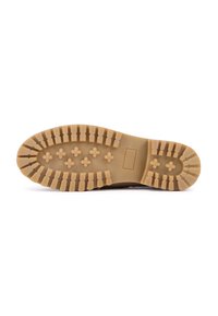 Semelle en caoutchouc d'une botte marron avec des crampons profonds et des motifs en forme de croix surélevés pour améliorer l'adhérence, présentée sur un fond blanc.