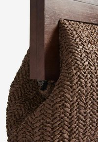 Cestino intrecciato marrone realizzato con fibre naturali, fissato a una struttura in legno scuro. Presenta una superficie testurizzata e una forma curva.