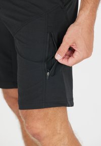Sorte shorts lavet af et letvægtsstof, med en lynlåslomme i siden og skrå sømdesign, samt en glat tekstur.