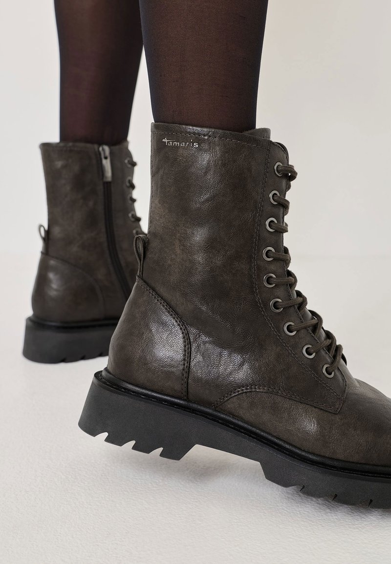 Gray lace-up ankle boots made of textured leather, featuring metal eyelets, a side zipper, and a rugged black sole with a serrated edge.