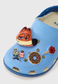 Tamanco azul-claro adornado com quatro charms temáticos de desenhos animados: uma cara de raposa, uma coelhinho correndo, um donut de chocolate com granulado e uma impressão de pata de pirulito vermelho.